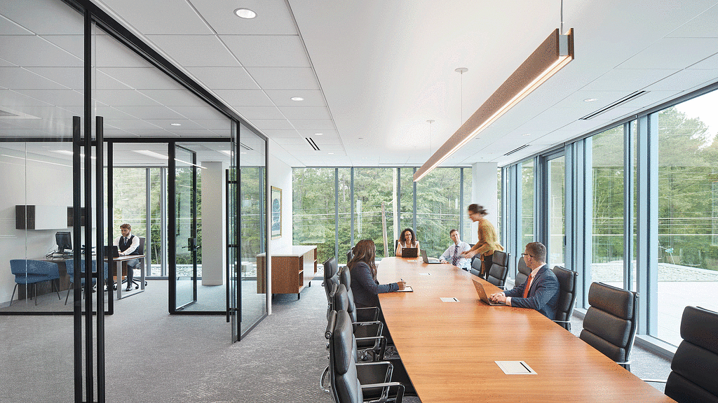 A group of people sitting around a table in a room with glass walls.