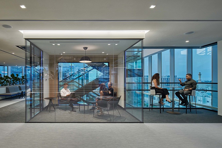 A group of people sitting at a table in a room with glass walls.
