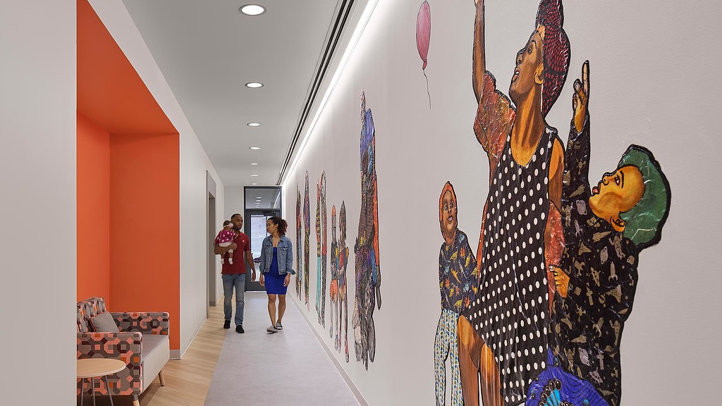 A couple of people walking down a hallway with a wall of kites.