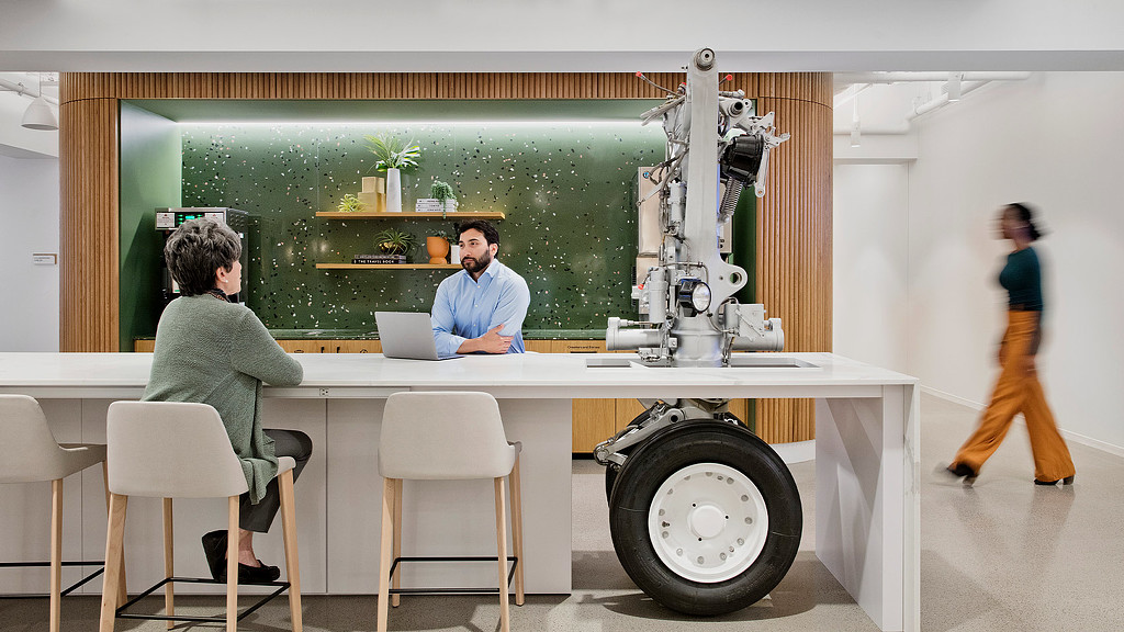A man and a woman sitting at a table with a laptop at United Airlines lounge with a airplane wheel