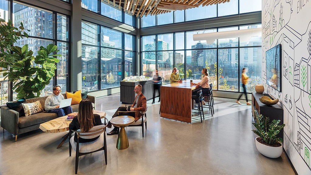 A group of people sitting in a room with windows and a table.