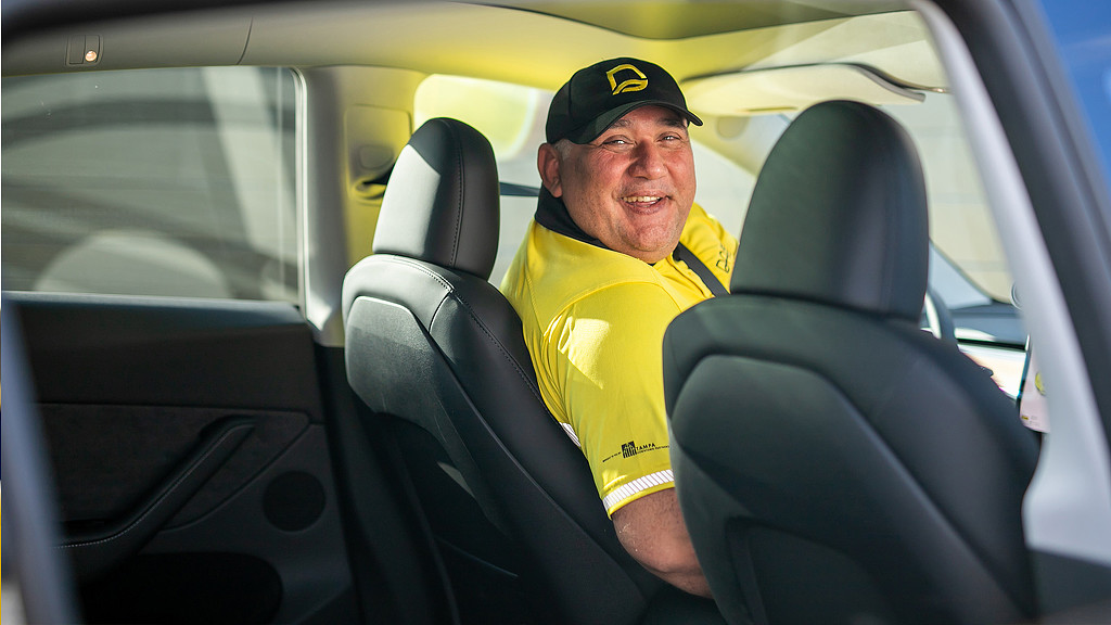 A man in the driver's seat of car wearing DASH branded shirt and hat
