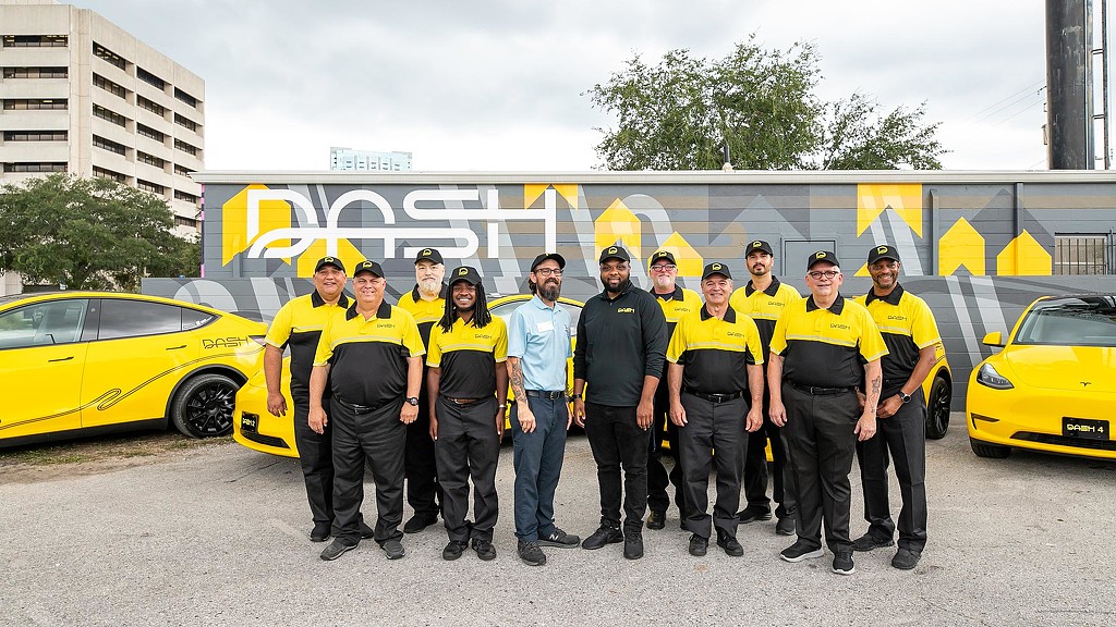 Group photo of team in DASH branded gear in front of yellow Teslas