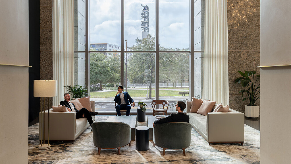 A couple of people sitting on a couch in a room with large windows.