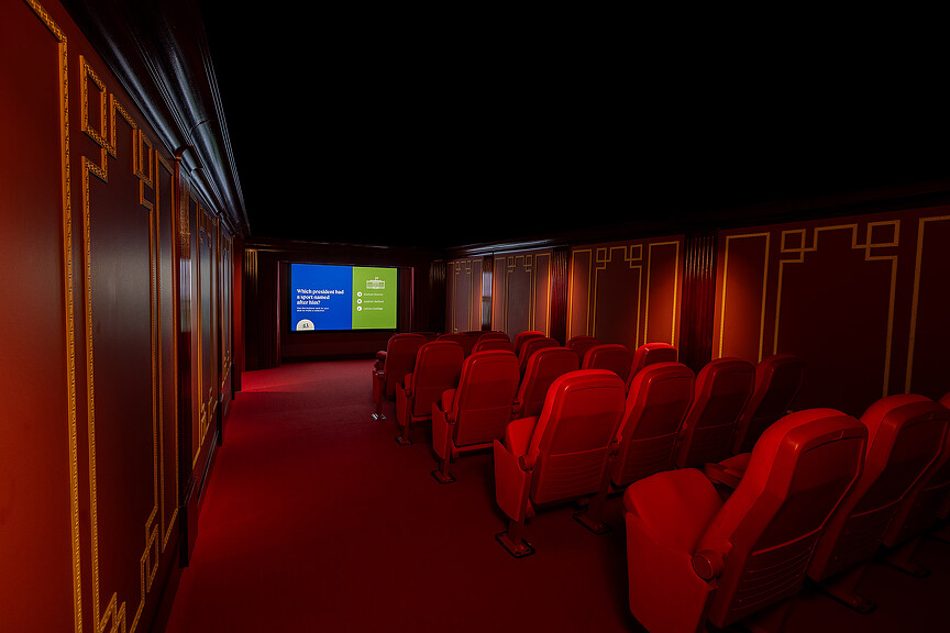A room with red chairs and a screen.