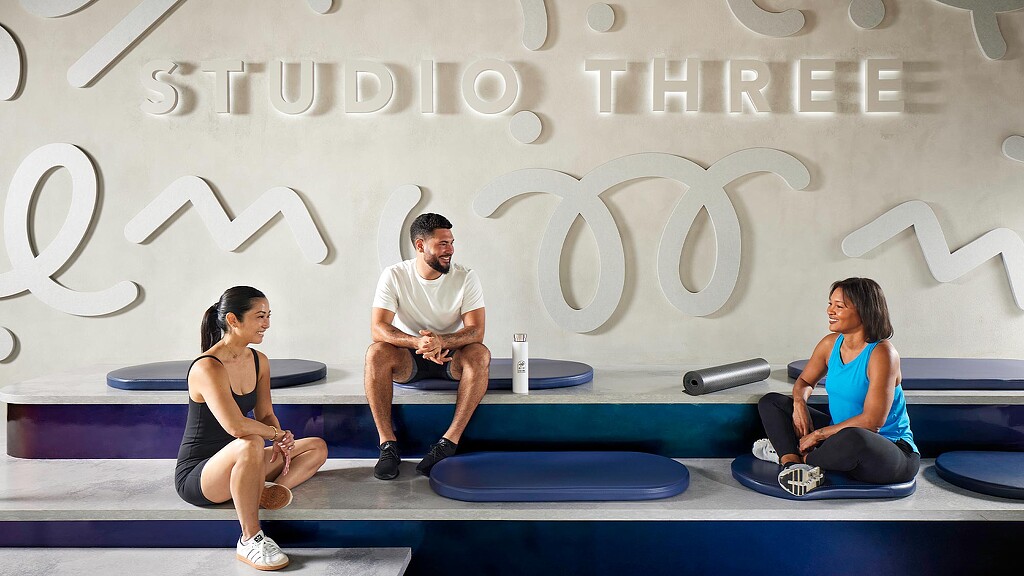 A man and woman sitting on a bench in front of a large screen.