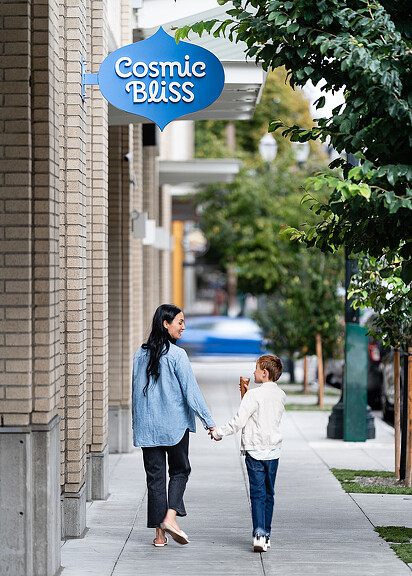 A woman and child walking down sidewalk under Cosmic Bliss sign
