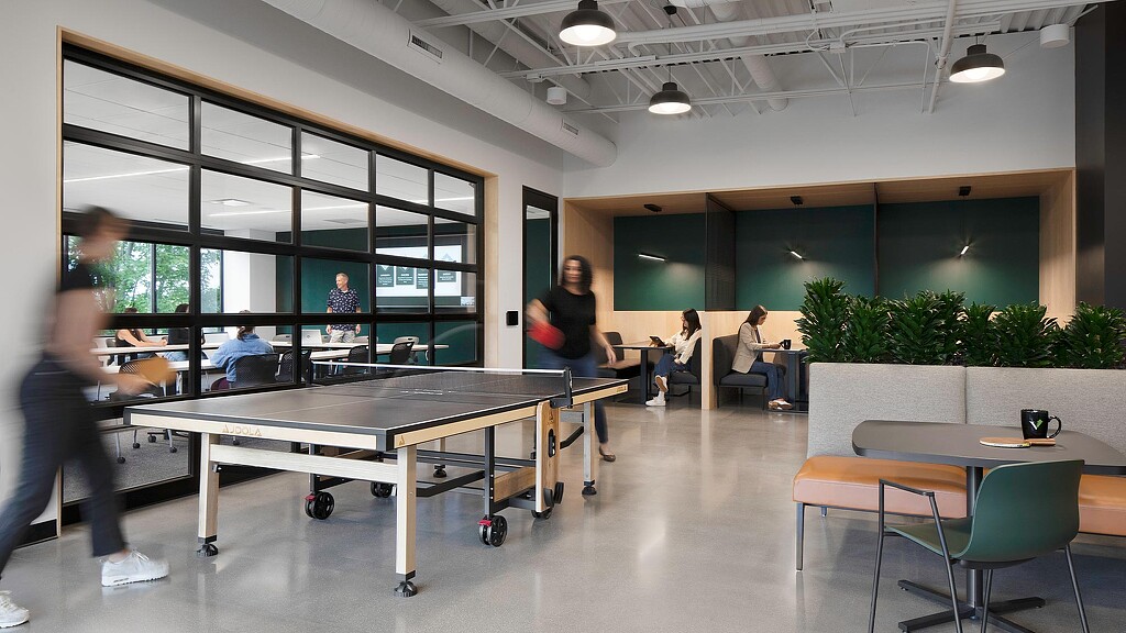 A group of people playing ping pong in a room with windows.