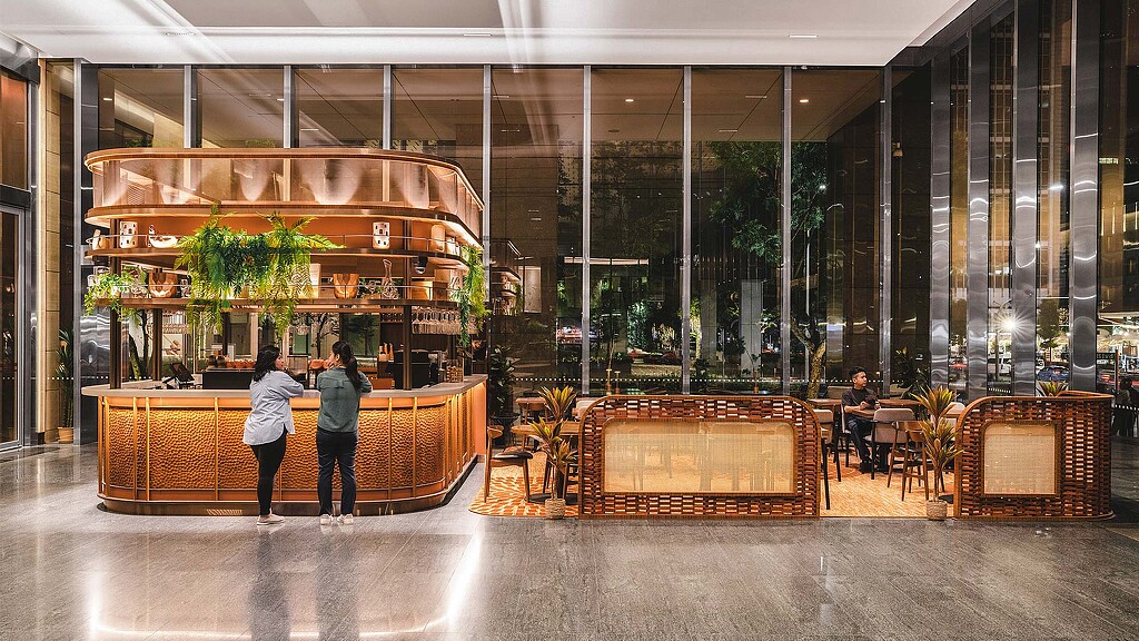 A group of people in a large room with glass walls and a large glass window with plants.