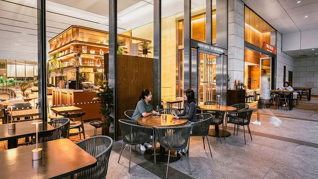 A couple of people sitting at a table in a large building.