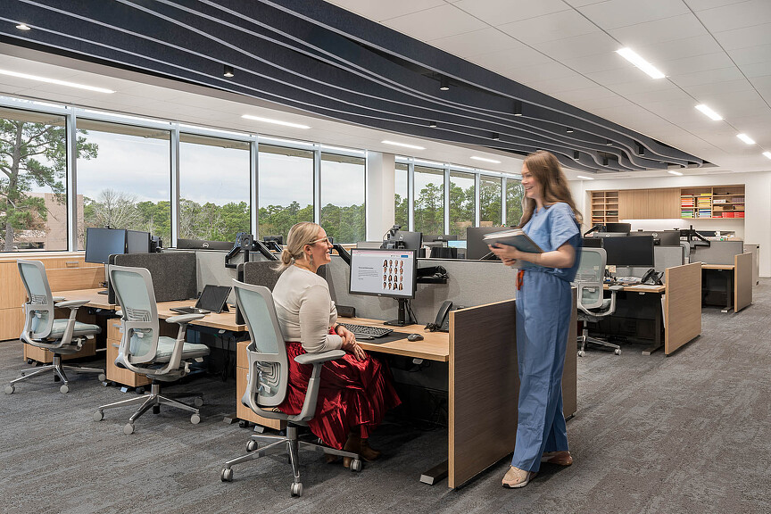 A person standing next to a person sitting at a desk.