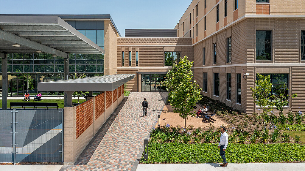 A courtyard with a brick walkway and a building with a tree and people.