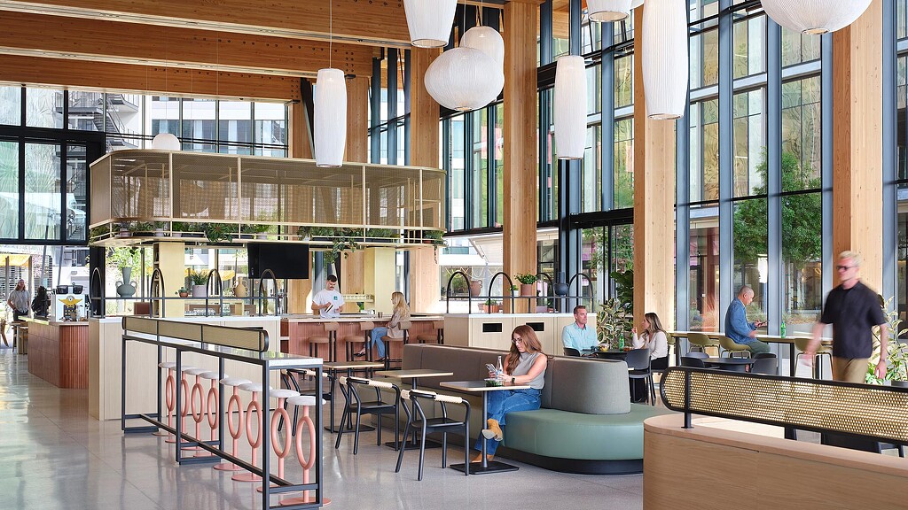 A group of people sitting at tables in a large room with windows.