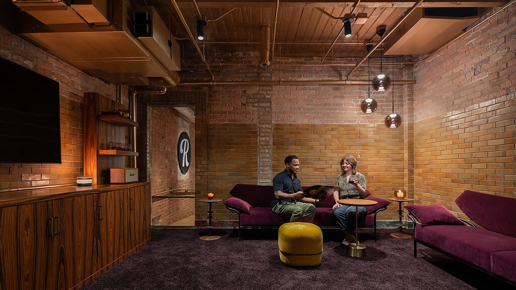 A man and woman sitting on a couch in a room with a brick wall and a tv.