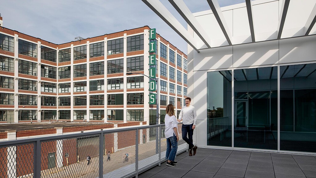 A man and woman walking on a bridge in front of a building.