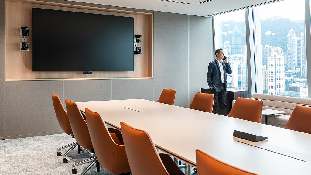 A person standing in front of a conference room table with a projector screen and chairs.