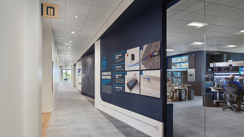 A person sitting at a desk in a room with a large screen.