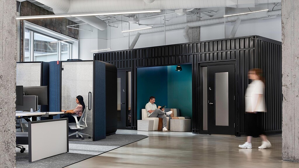 A woman standing in a room with a man sitting on a chair.