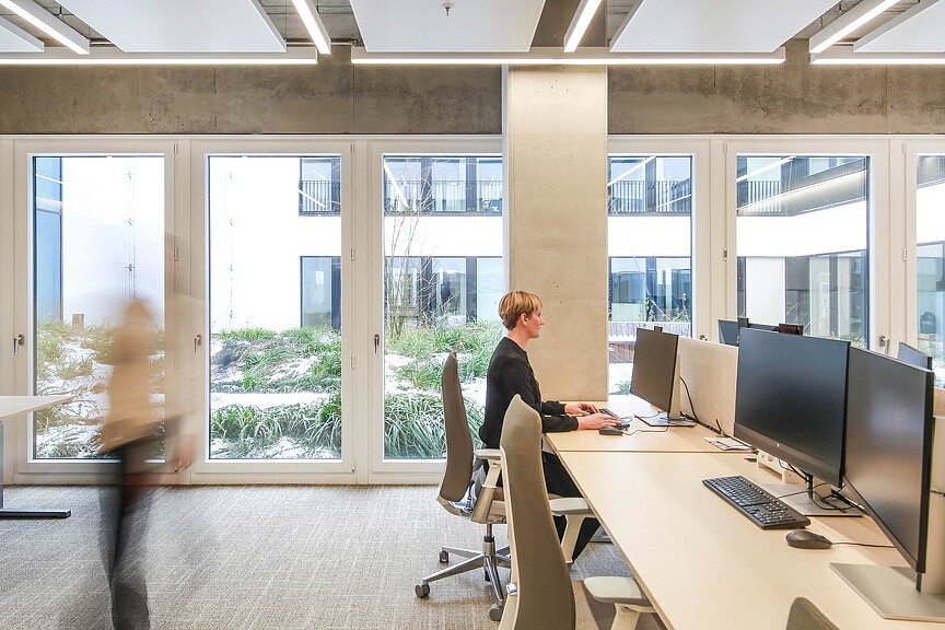 A person sitting at a desk with a computer and a large window.