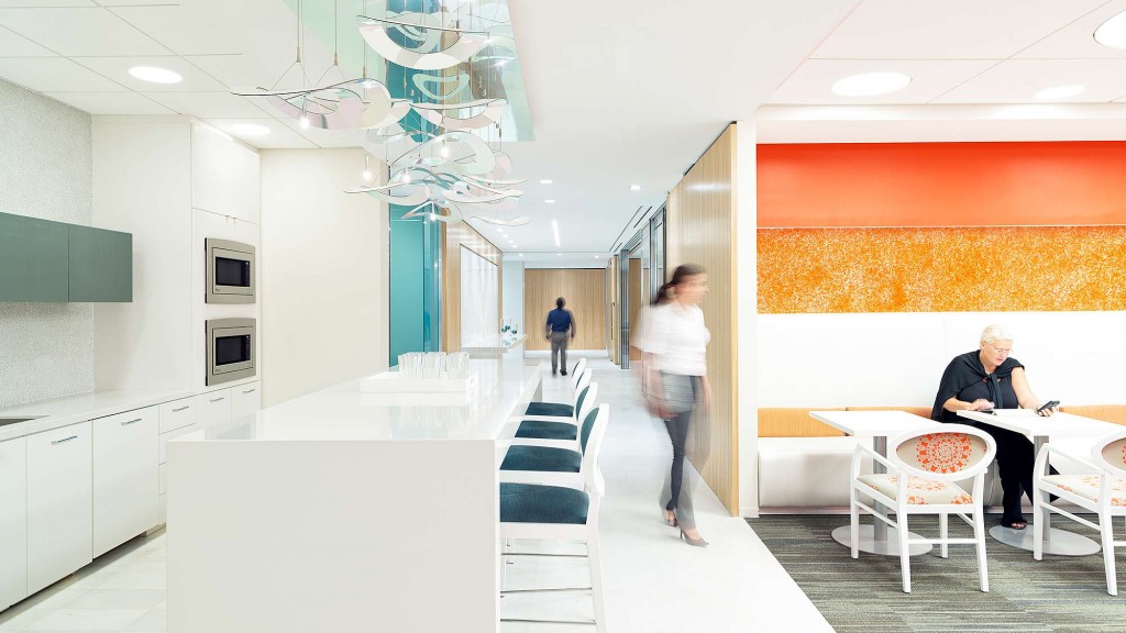 A man and woman walking down a hall with a man sitting at a table.