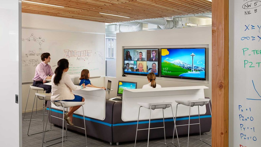 A group of people sitting at a table in a room with a large screen.
