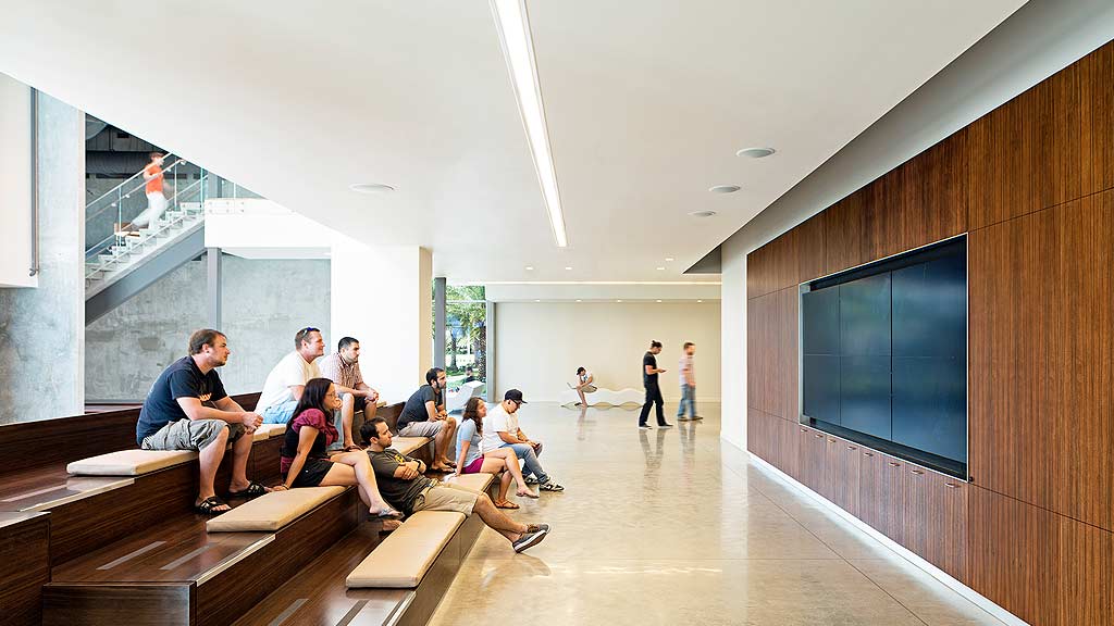 A group of people sitting on benches in a room with a large screen.