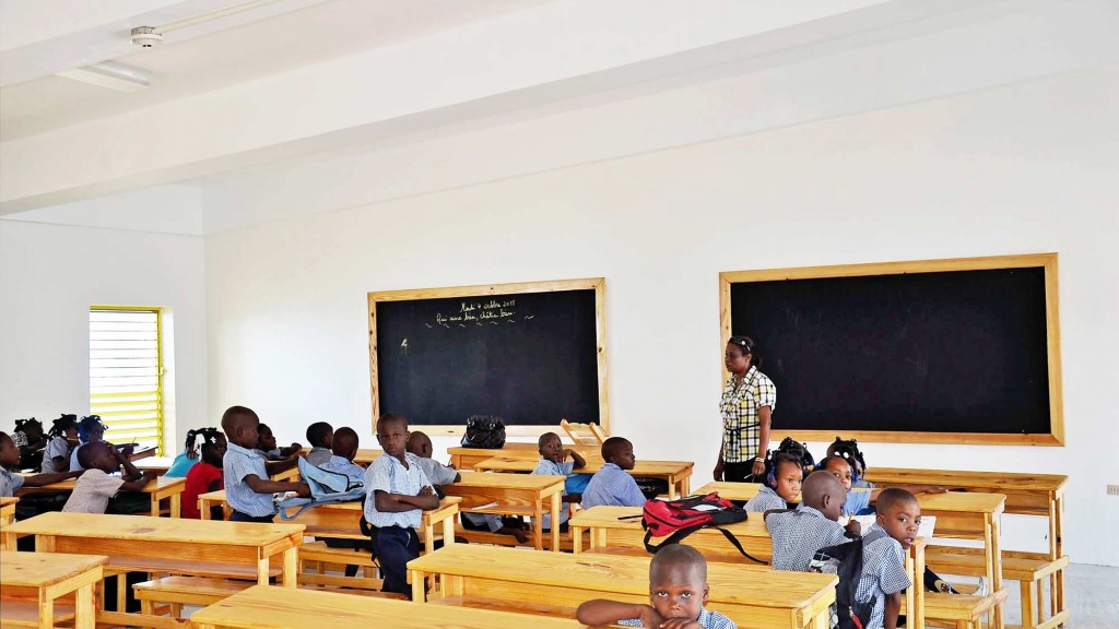 A classroom with students and a person standing in front of a screen.