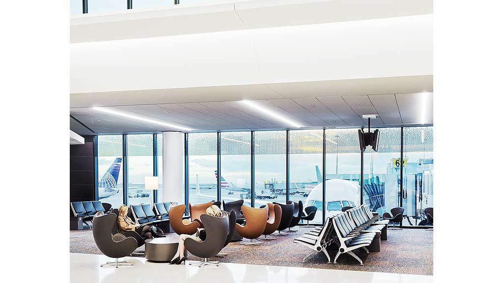 A room with a large window and chairs with a body of water in the background.