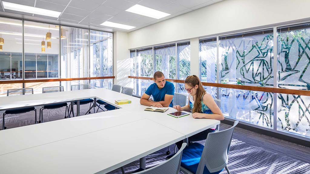 A man and a woman sitting at a table in a room with windows.