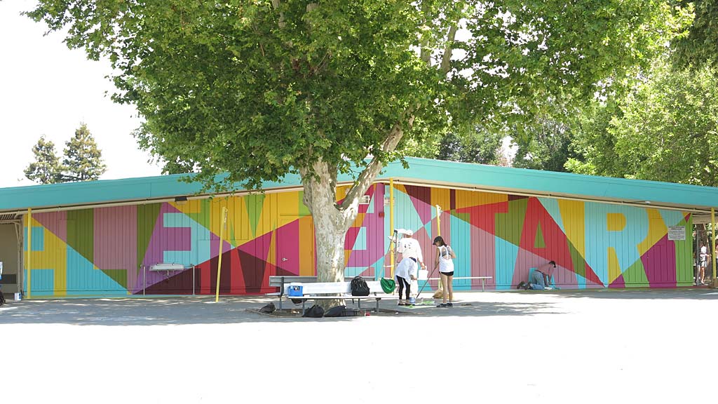A group of people standing outside a building with a tree in front.
