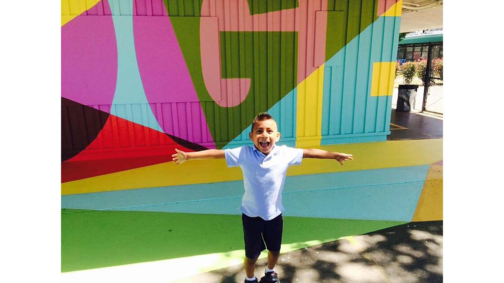 A boy standing in front of a colorful wall.