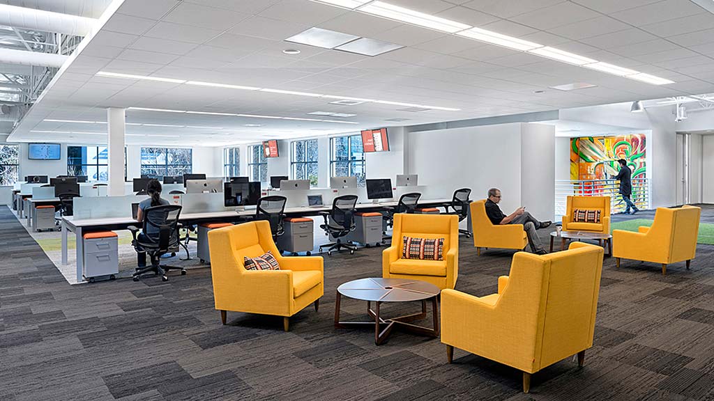 A room with yellow chairs and a person sitting at a desk with a computer.