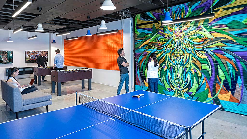 People playing ping pong in a room with a wall of art.