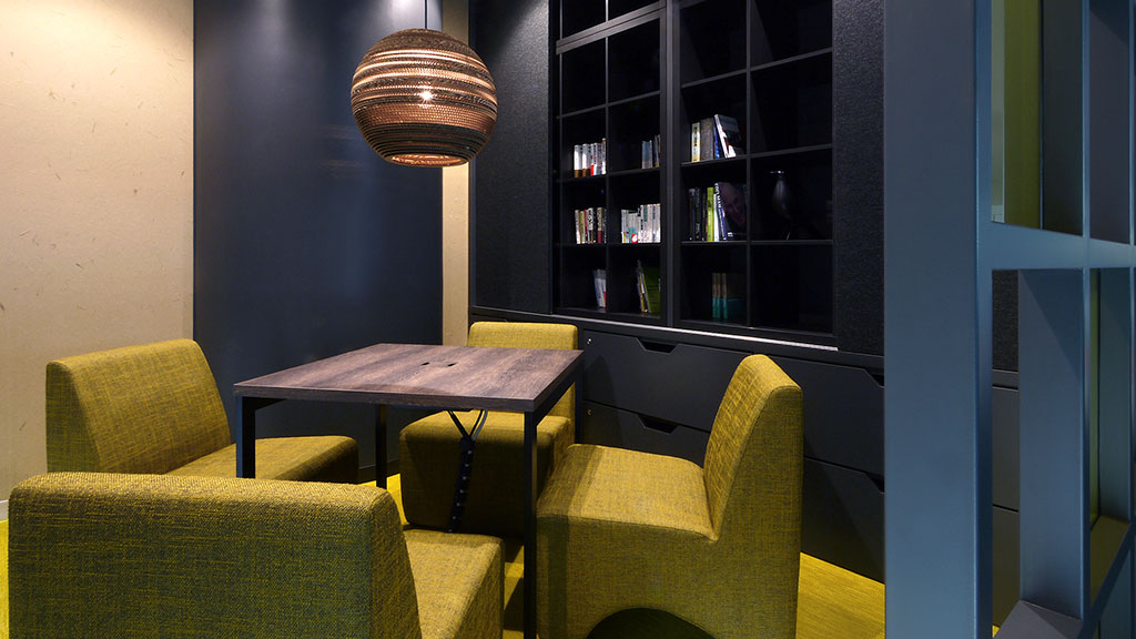 A room with green chairs and a table with a lamp on it.