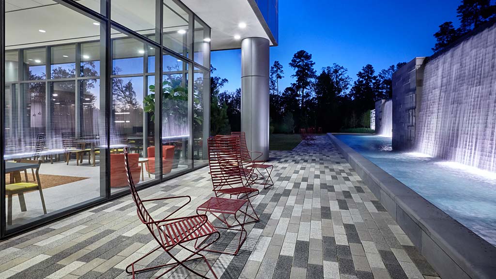 A patio with chairs and a covered patio with a large glass wall.