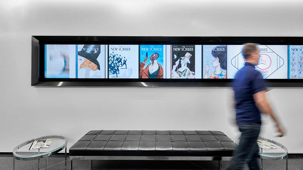 A man walking in front of a wall of pictures.