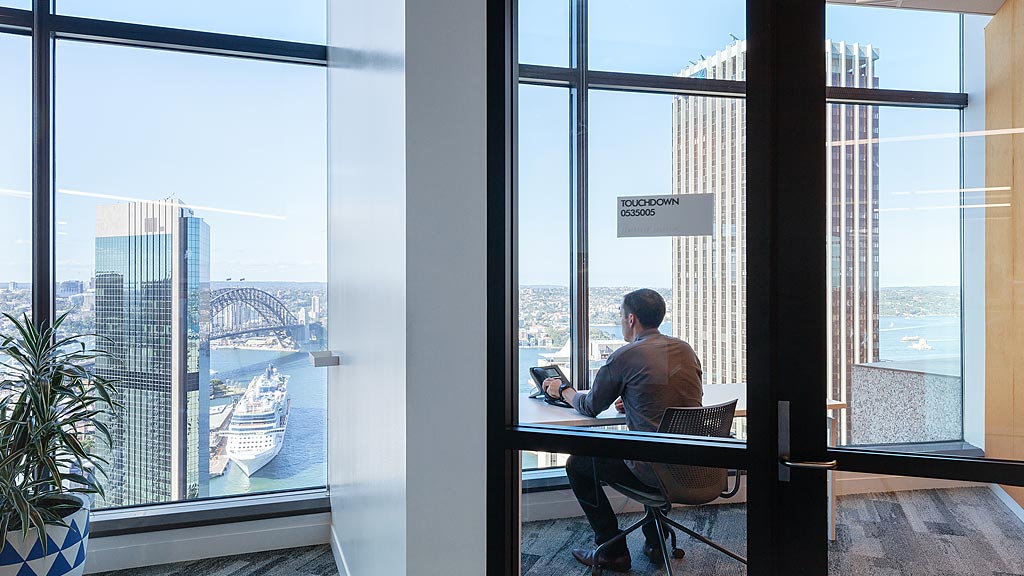 A person sitting at a table with a laptop in front of a window.