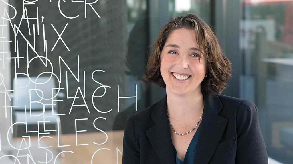 A person smiling in front of a chalkboard.