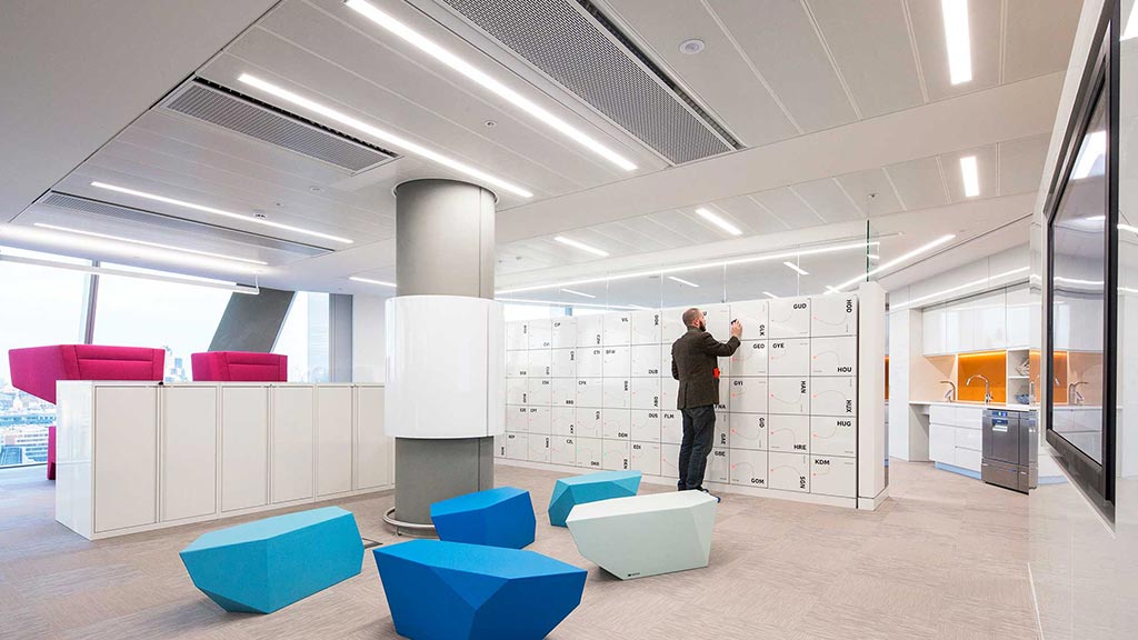 A person standing in a room with white cabinets and blue chairs.