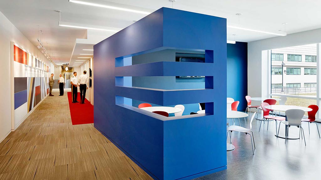 A room with a blue wall and chairs and people standing around.