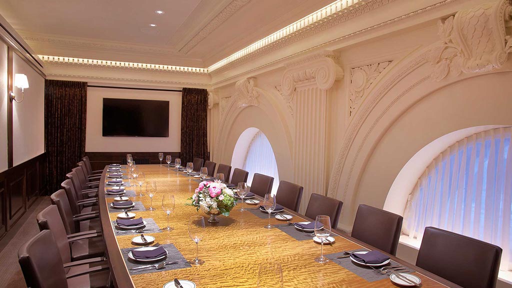 A dining room table with a tv on the wall.