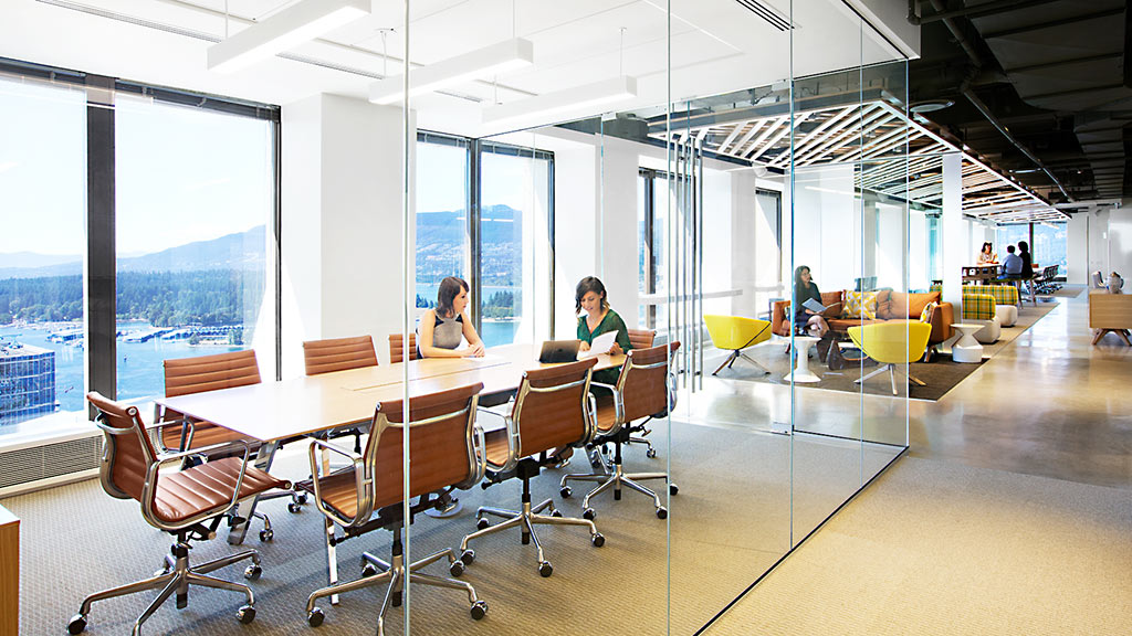 A group of people sitting at a table in a large room with large windows.