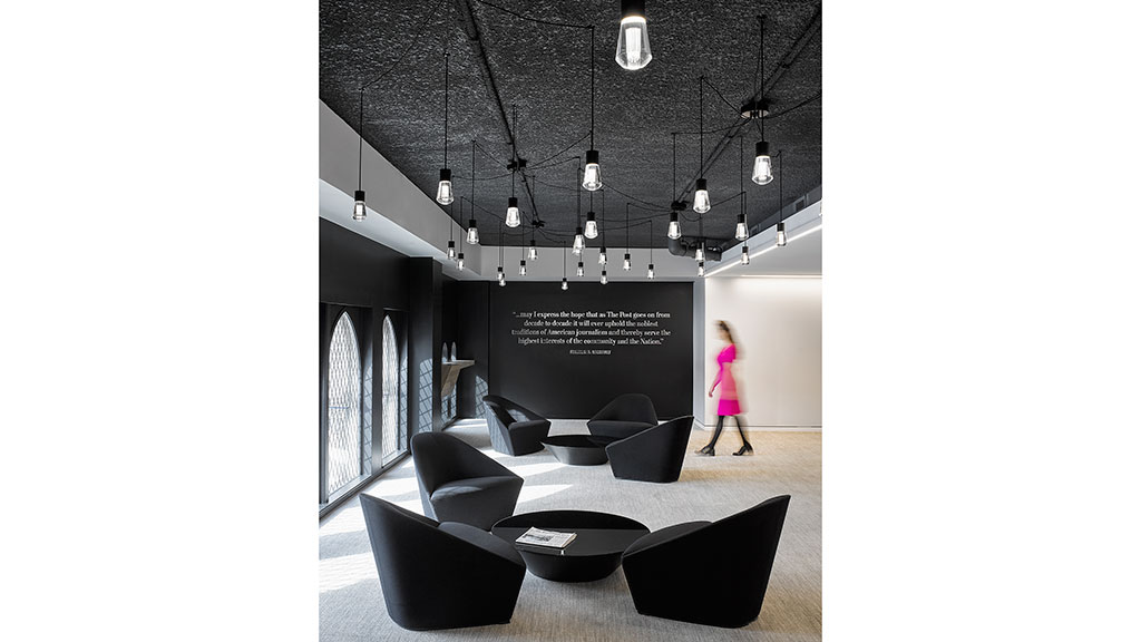 A person standing in a room with a large screen and chairs.