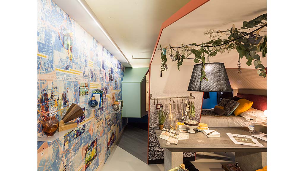 A room with a desk and a lamp and a wall with art.