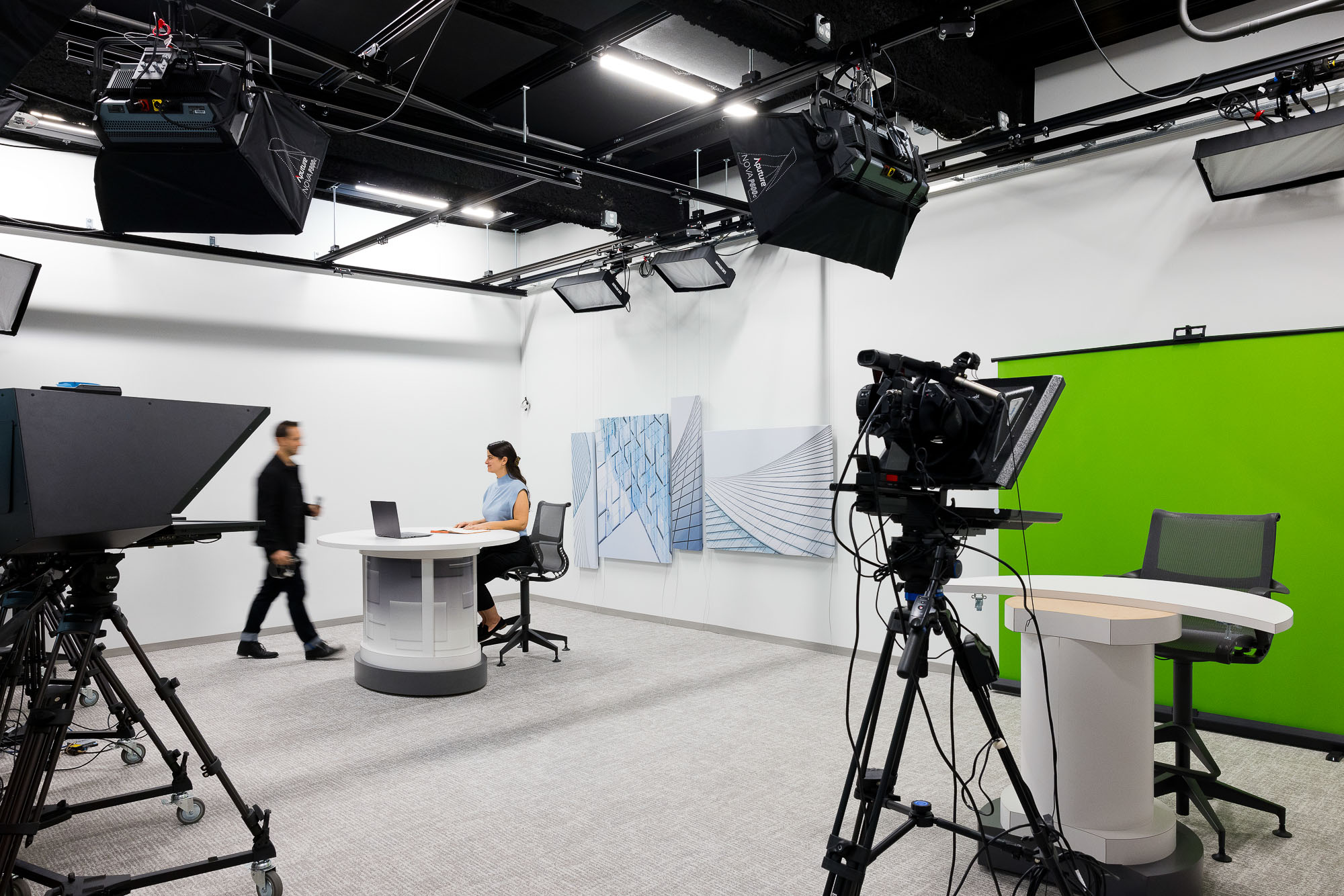 A person standing in a room with a camera and a person sitting at a desk with a camera.