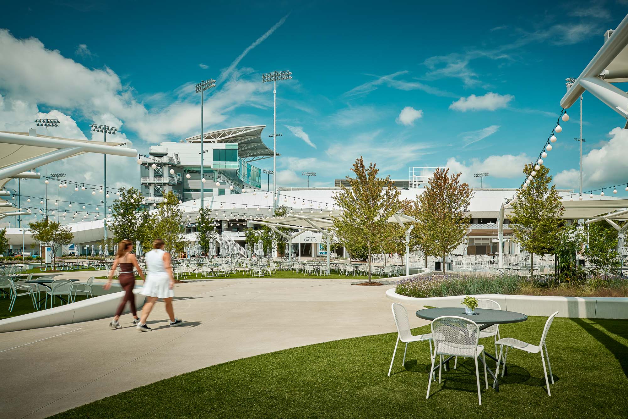 A couple of women walking on a grass lawn with a ferris wheel in the background.