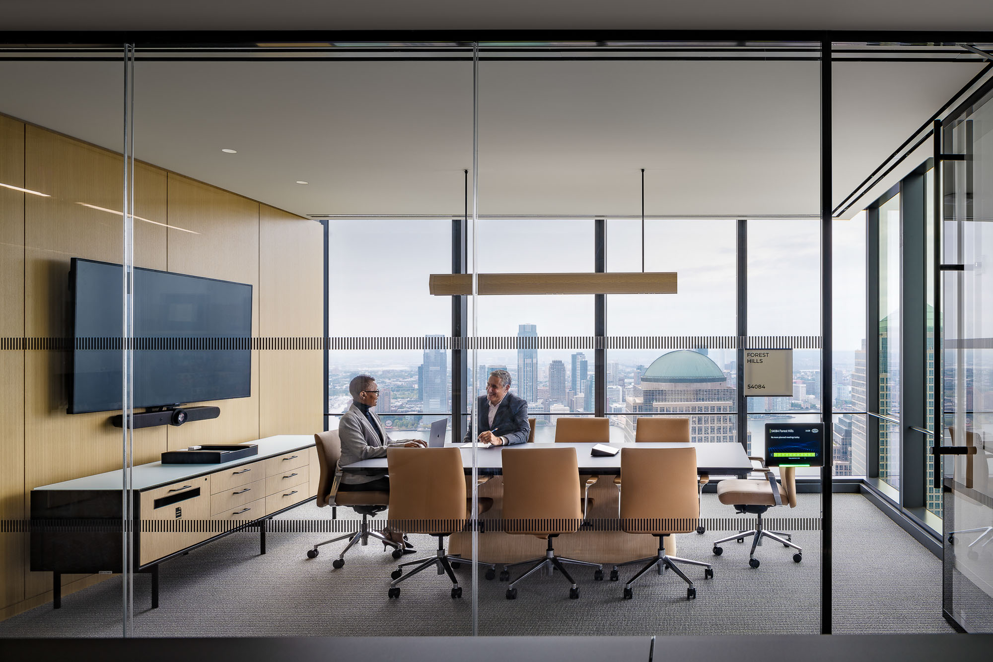 A couple of people sitting at a table in a room with large windows.