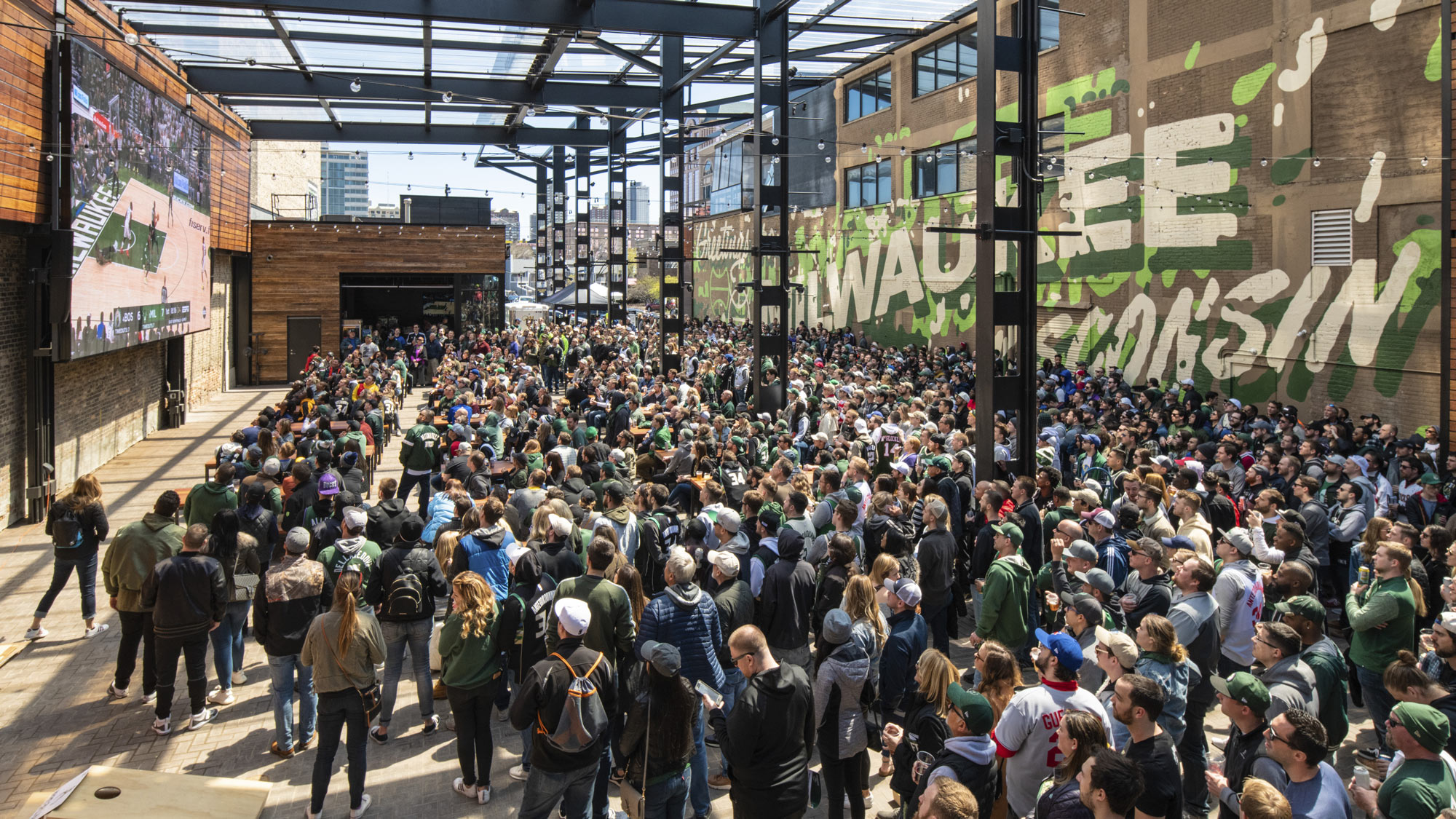 A crowd of people walking on a street with a stage and a large screen.