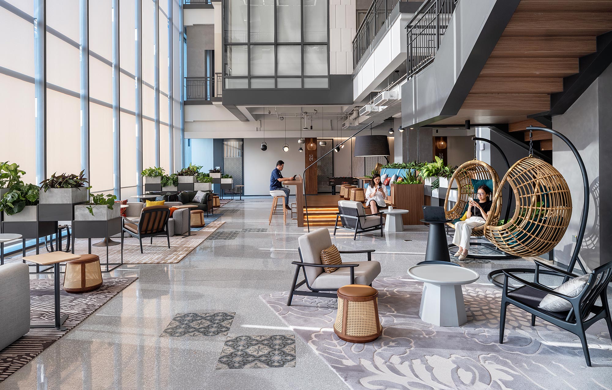 A group of people sitting at tables in a large room with windows.