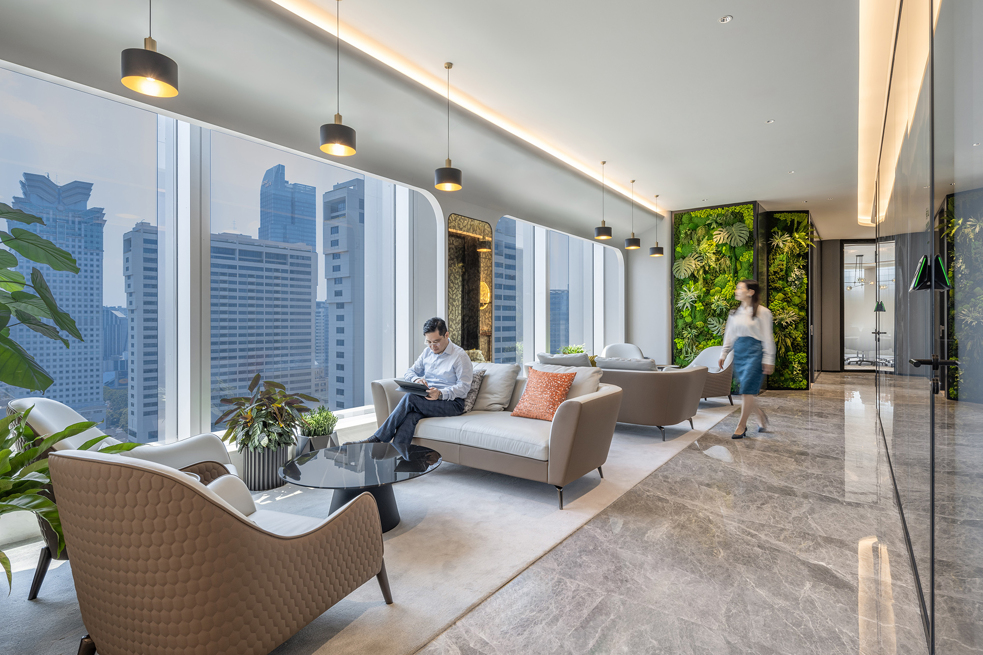 A man and woman sitting on a couch in a room with a large window and a large city.